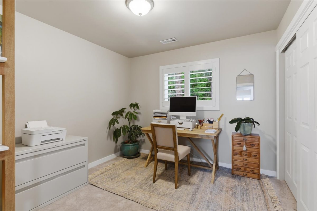 Bright interior room featuring a window with white plantation shutters, neutral wall paint, overhead flush-mount lighting, and light-toned carpet flooring