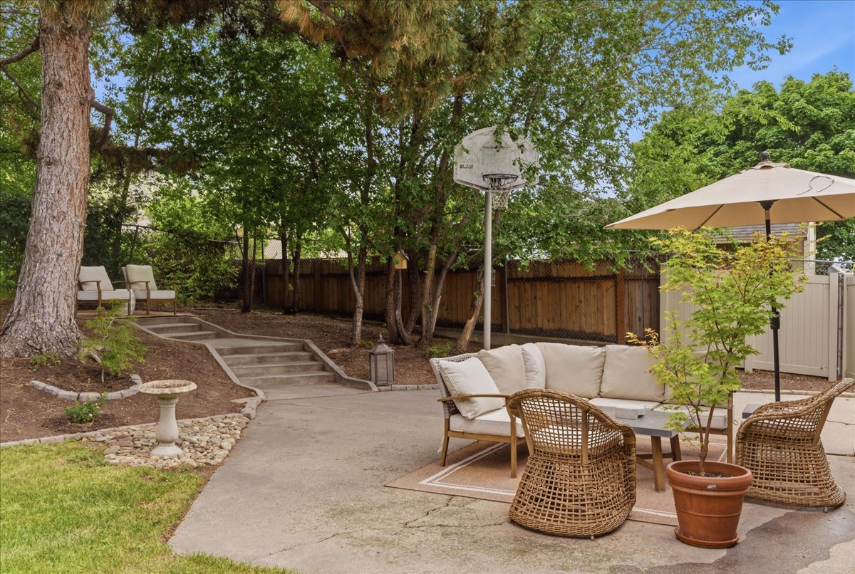 Private outdoor space featuring mature trees, concrete patio, multi-level landscaping with concrete stairs, and perimeter fencing