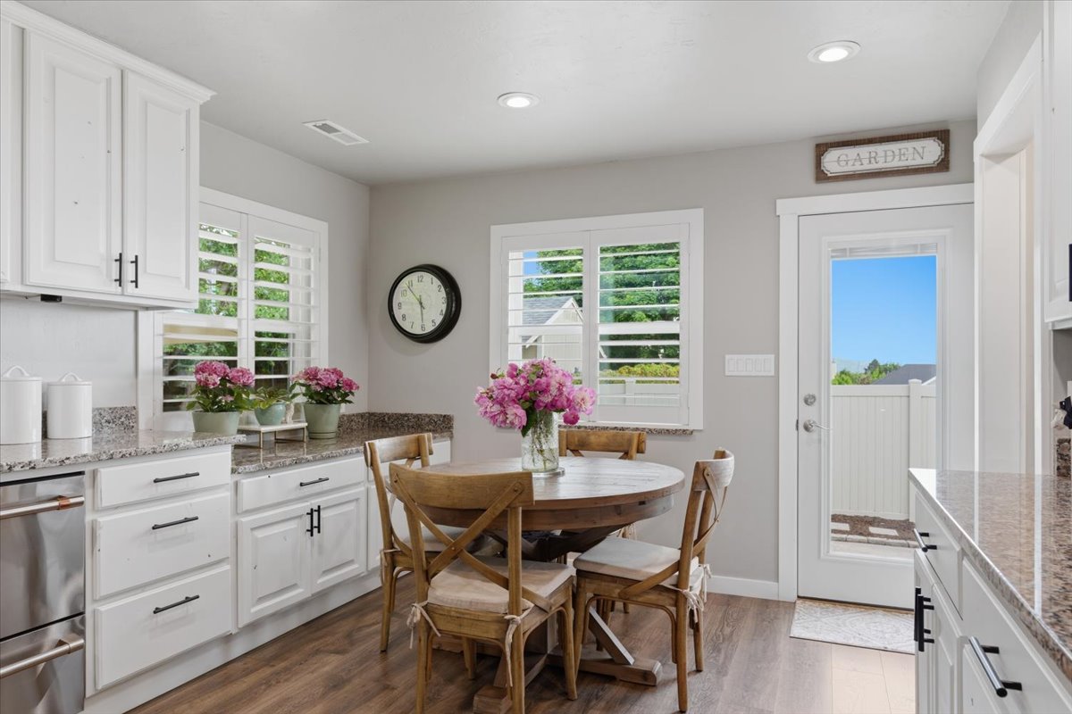 Kitchen dining area featuring white cabinetry, granite-style countertops, stainless steel appliances, wood-finish flooring, and a glass-paneled exterior door