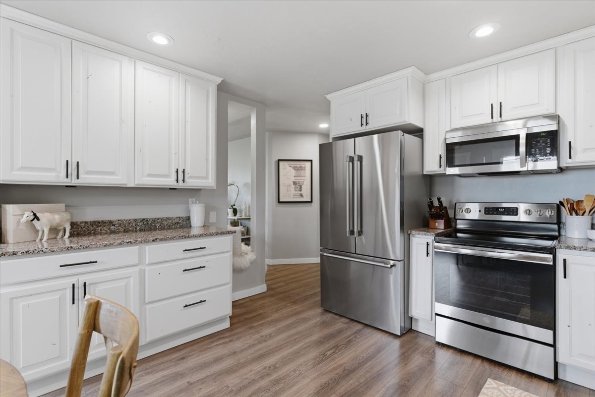 Kitchen featuring white shaker cabinetry with dark hardware, granite-style countertops, and wood-finish flooring