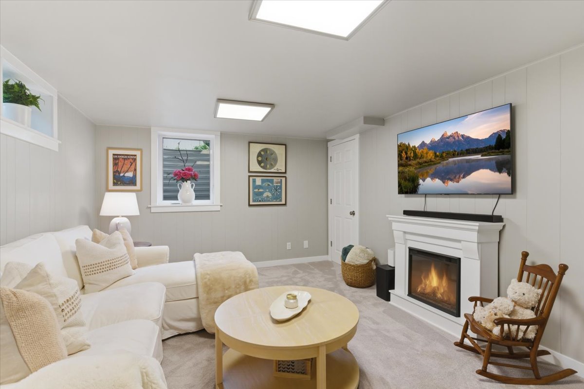 Carpeted living space featuring a fireplace with a white mantel, two rectangular ceiling-mounted light fixtures, and paneled wall finishes