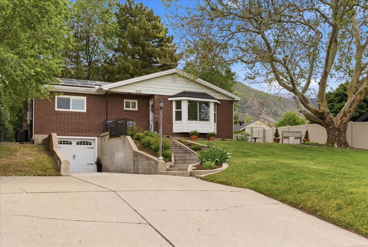 Traditional brick residence featuring a large front lawn, mature trees, a multi-pane bay window, solar panels, and a lower-level garage