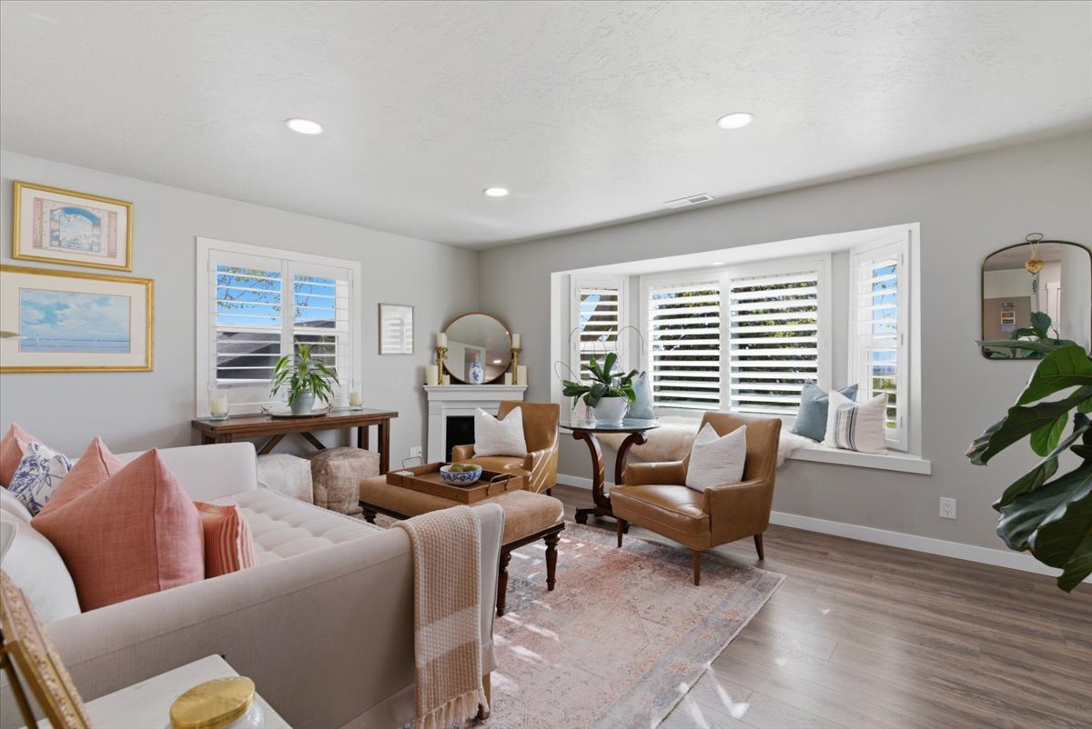 Living area featuring light gray wall tones, recessed lighting, wood-finish flooring, a bay window with plantation shutters, and a decorative fireplace