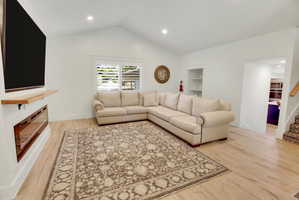 Spacious living area featuring light wood-finish flooring and a vaulted ceiling with recessed lighting