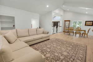 Open-concept living area featuring light wood-finish flooring, vaulted ceilings, recessed lighting, and white plantation shutters
