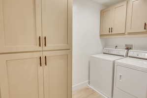 Laundry area featuring light-toned cabinetry with dark hardware, a pair of white appliances, and light wood-finish flooring