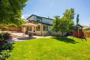Expansive backyard featuring a lush lawn, a multi-level patio area, mature trees, and a wooden privacy fence