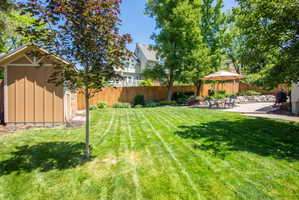 Expansive backyard featuring a large green lawn, concrete patio, privacy fencing, and a built-in storage shed