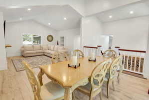 Open-concept dining and living areas featuring vaulted ceilings, recessed lighting, and wood-finish flooring