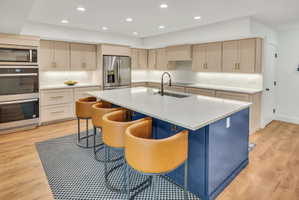 Spacious kitchen featuring a large blue island, light-toned cabinetry, stainless steel appliances, wood-finish flooring, and recessed lighting