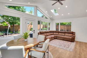Vaulted ceiling sunroom featuring multiple large windows, a skylight, recessed lighting, a ceiling fan, and wood-finish flooring