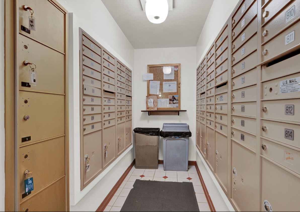 Well-lit mailroom featuring extensive wall-mounted mailboxes and a central bulletin board