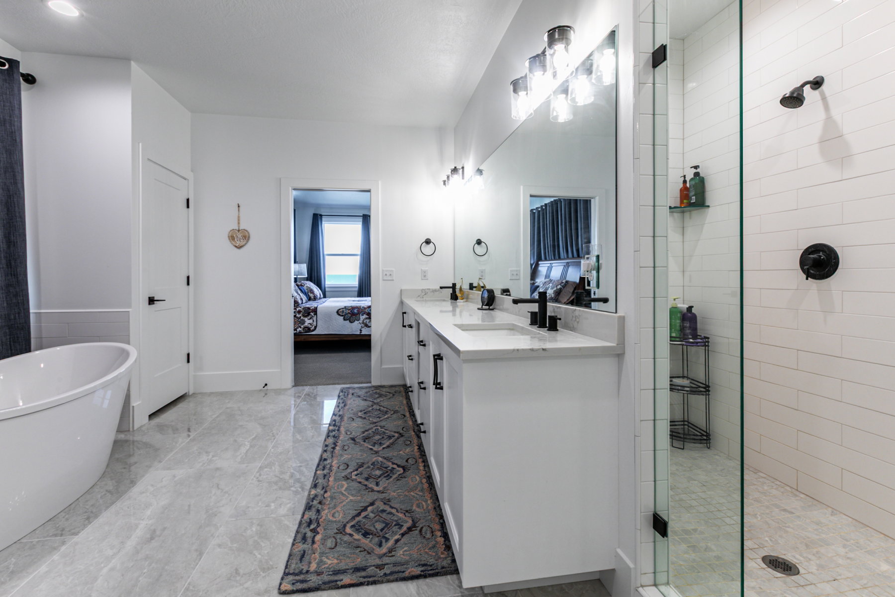 Contemporary bathroom featuring a freestanding tub, dual vanity with undermount sinks and black fixtures, and a glass-enclosed shower with subway tile surround