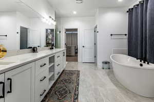Spacious bathroom featuring a freestanding soaking tub, an extended vanity with white cabinetry, light-toned countertops, and large format floor tiling