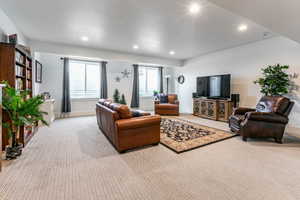 Spacious living area featuring recessed lighting, light-toned patterned carpeting, and dual windows with privacy blinds