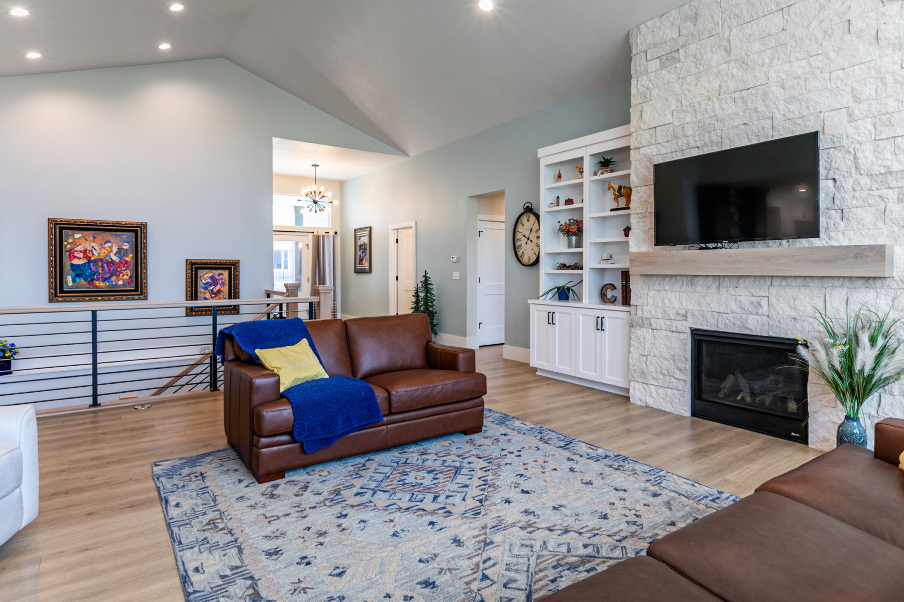 Spacious living area featuring a vaulted ceiling with recessed lighting, stone-clad fireplace with mantel, built-in shelving, and wood-finish flooring