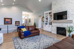 Spacious living area featuring a vaulted ceiling with recessed lighting, stone-clad fireplace with mantel, built-in shelving, and wood-finish flooring