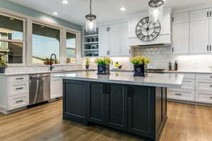 Expansive kitchen featuring a large central island with dark cabinetry and light-toned countertops, white perimeter cabinetry, wood-finish flooring, and a white subway tile backsplash
