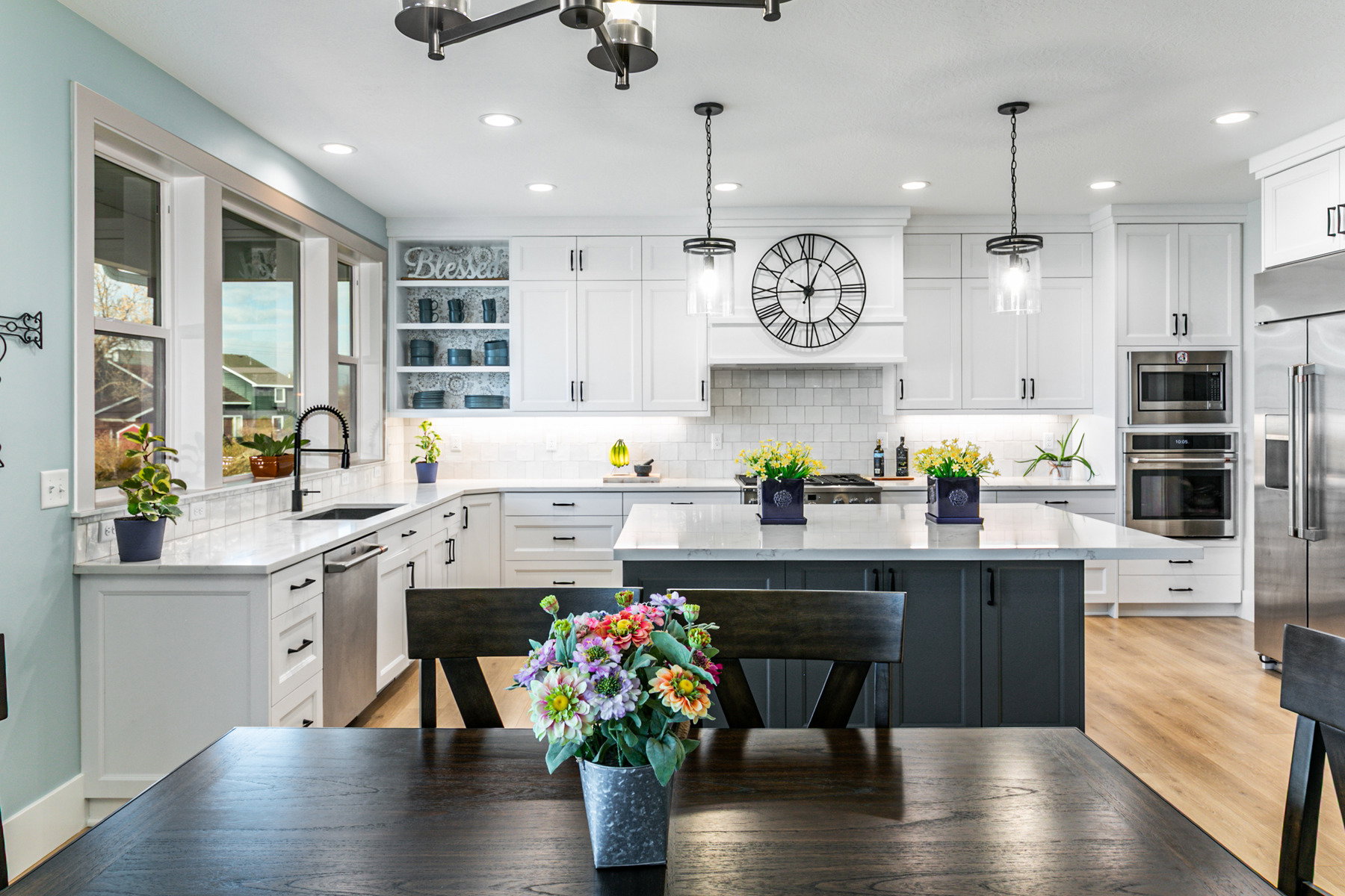 Modern kitchen featuring an expansive island with a light-toned countertop, white cabinetry with dark hardware, stainless steel appliances, wood-finish flooring, and pendant lighting fixtures