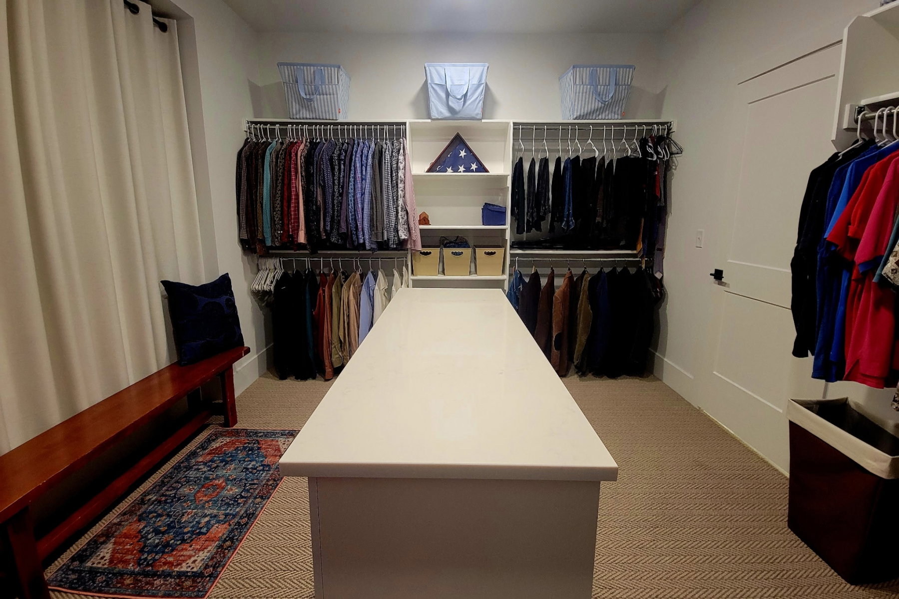 Custom closet system featuring a central island with a solid surface countertop, multiple hanging rods, integrated shelving, and neutral tone carpeting