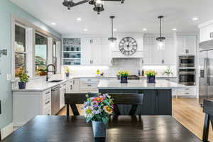 Open-concept kitchen featuring white shaker-style cabinetry, a contrasting dark gray island with a light-toned countertop, stainless steel appliances, and wood-finish flooring