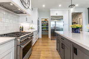 Gourmet kitchen featuring a stainless steel range with overhead ventilation, white shaker cabinetry, light-toned countertops, a stainless steel refrigerator, and wood-finish flooring