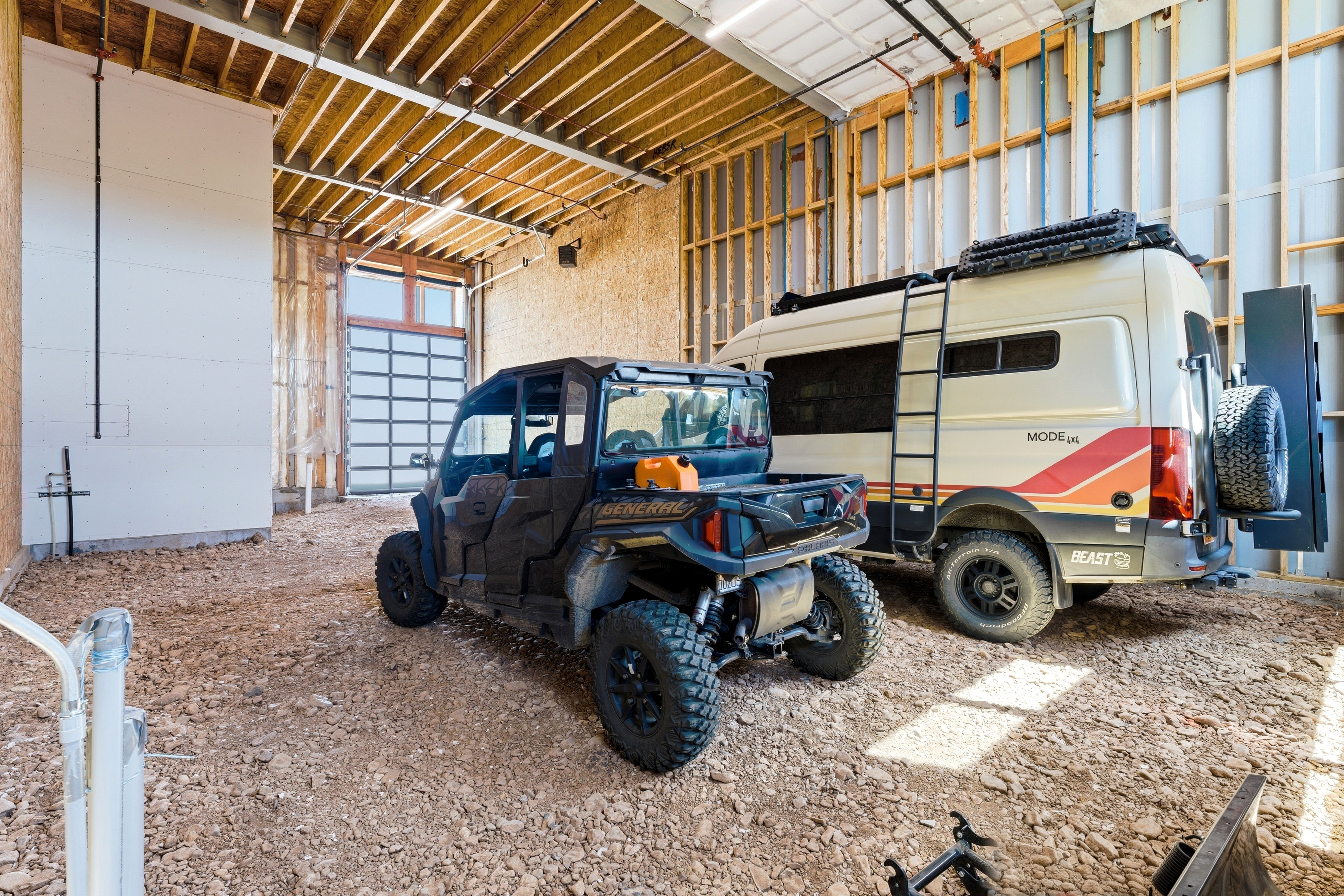 Spacious interior featuring exposed wood framing, an overhead garage door with upper transom window, and a gravel floor