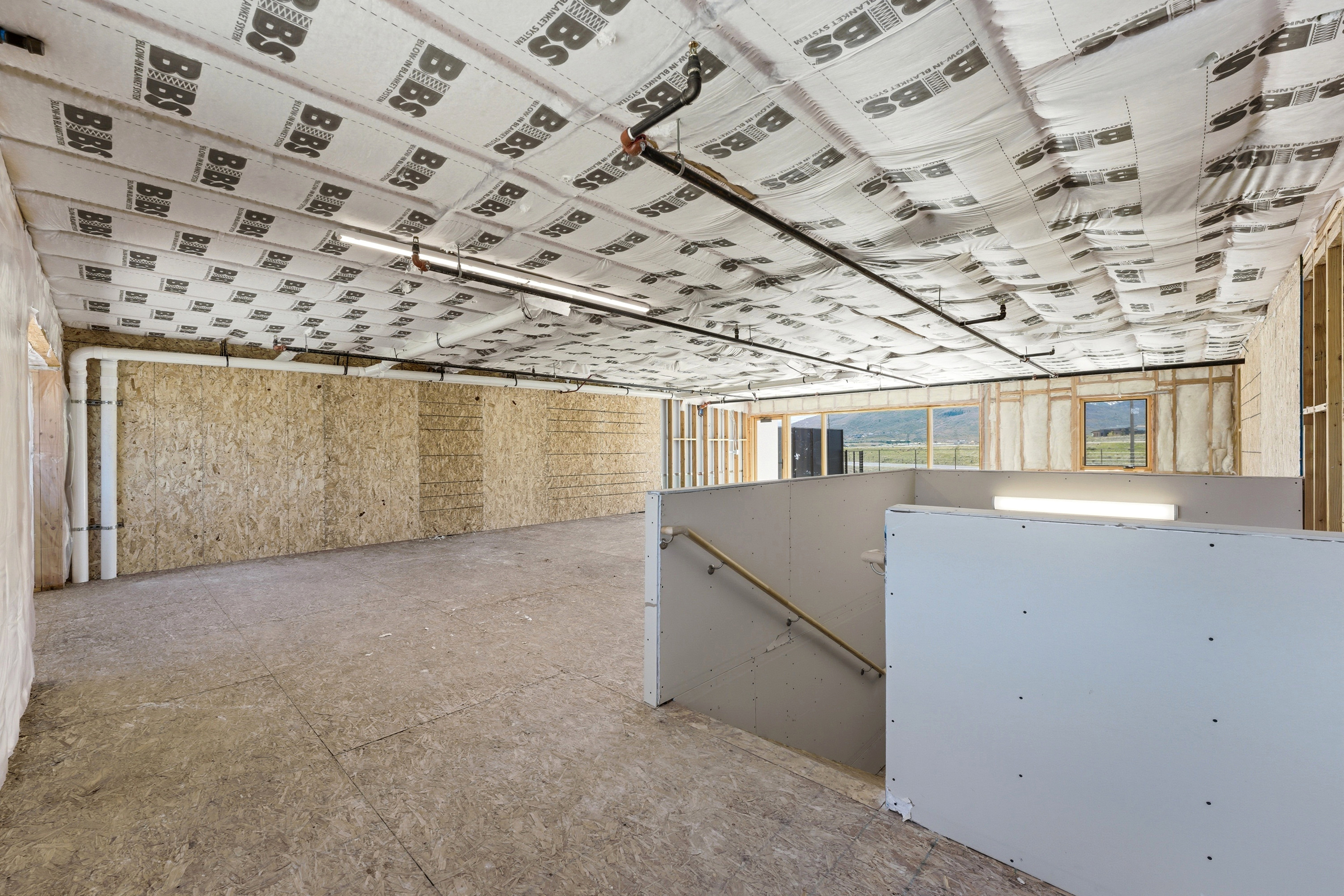 Spacious unfinished basement with exposed ceiling insulation, visible plumbing, and electrical lines