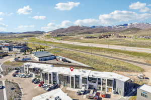 Modern commercial building with a grey and white facade, multiple roll-up garage doors, ample on-site parking, and immediate proximity to a major highway