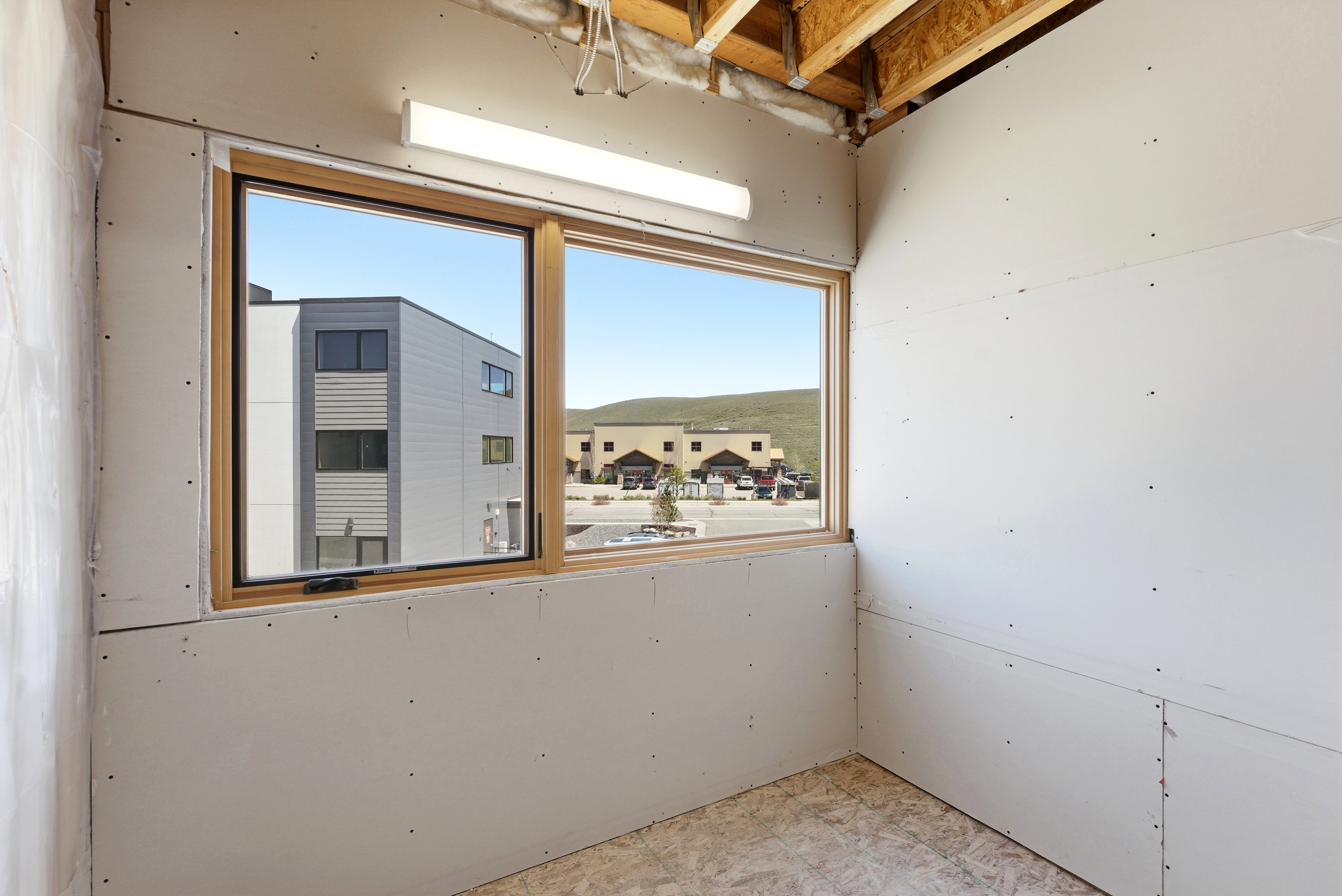 Room under construction featuring drywall installation, unfinished wood-finish flooring, and exposed ceiling joists