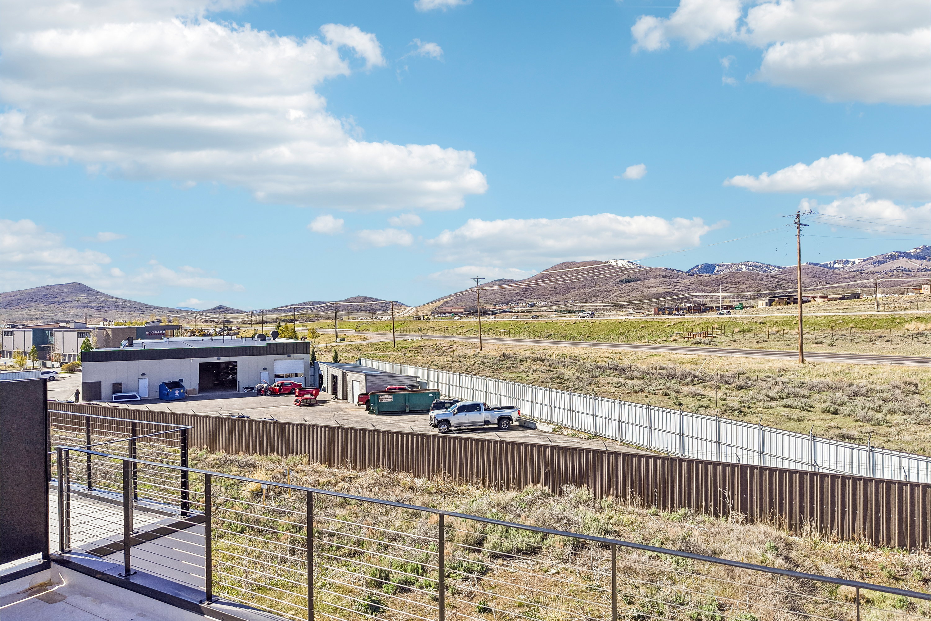 Spacious outdoor balcony with cable railing system overlooking a commercial building with multiple bay doors and a large paved area