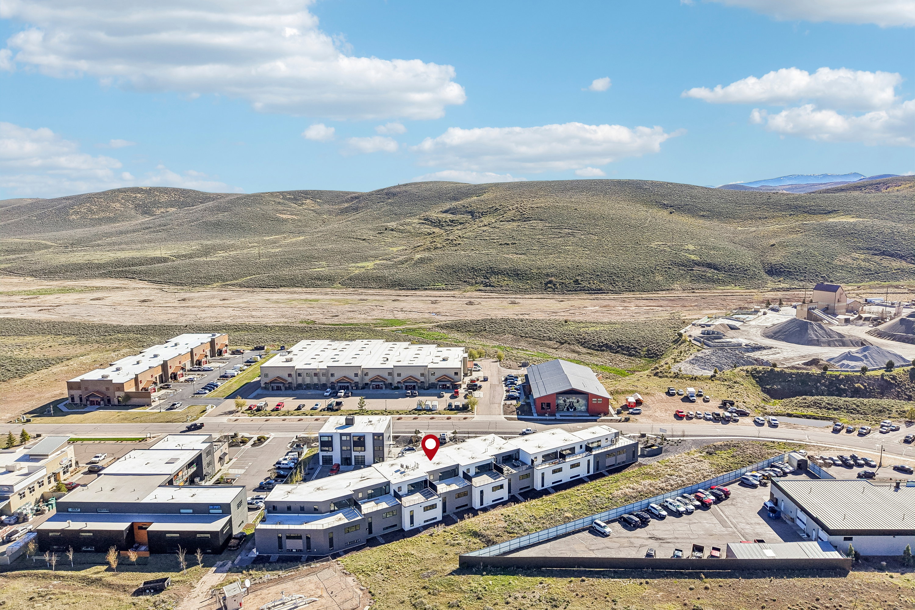 Modern multifamily residential buildings with distinct architectural designs, surrounded by expansive undeveloped hills