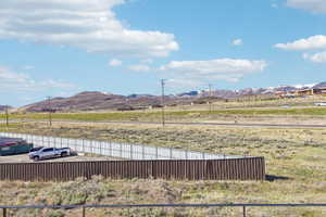 Expansive undeveloped land featuring a partial perimeter fence, a brown corrugated metal retaining wall, and distant snow-capped mountains