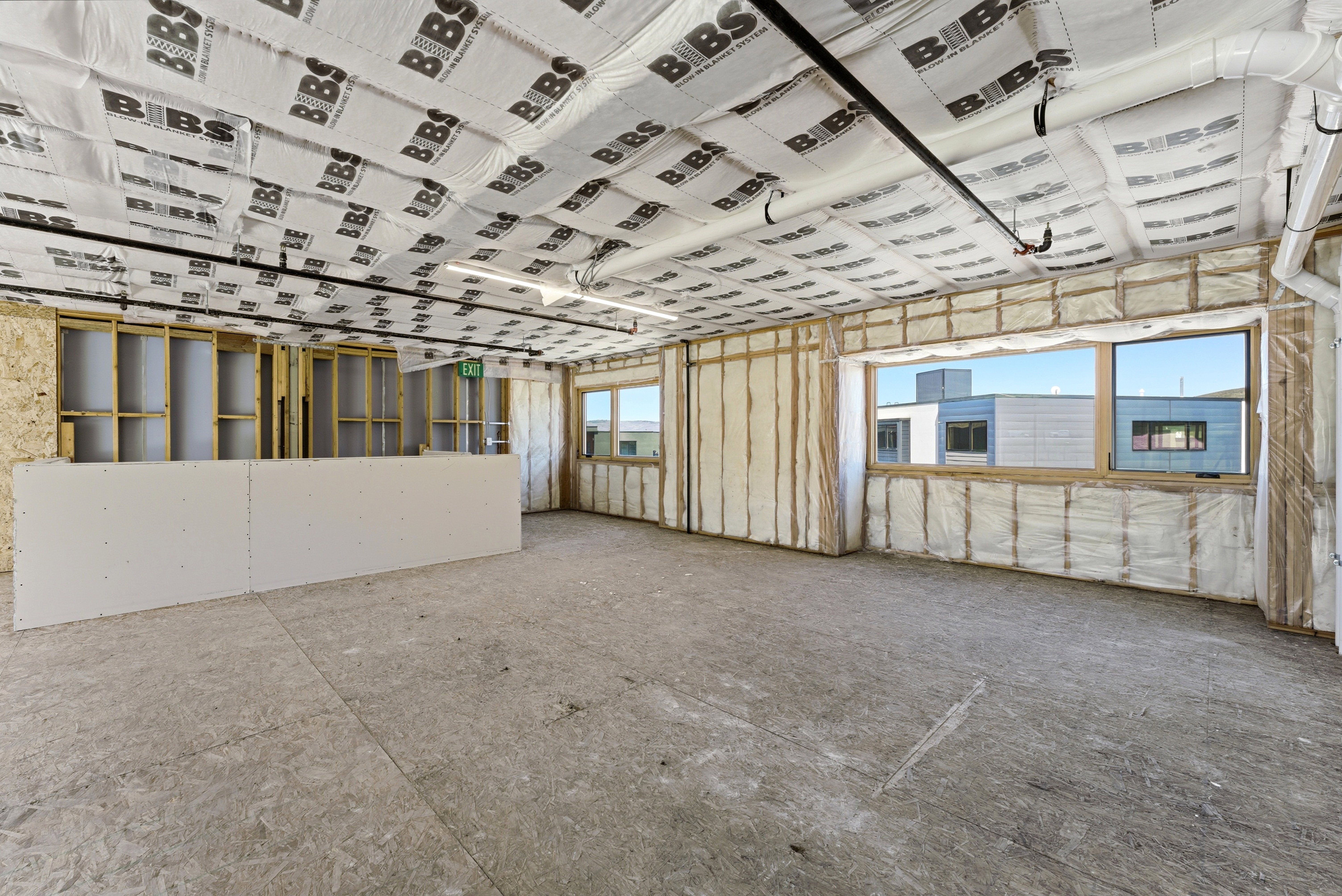 Open-concept space featuring exposed ceiling joists with insulation, a partial drywall partition, and two large windows