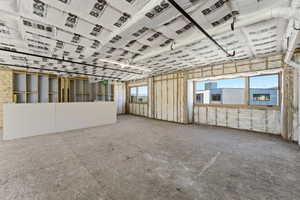 Open-concept space featuring exposed ceiling joists with insulation, a partial drywall partition, and two large windows
