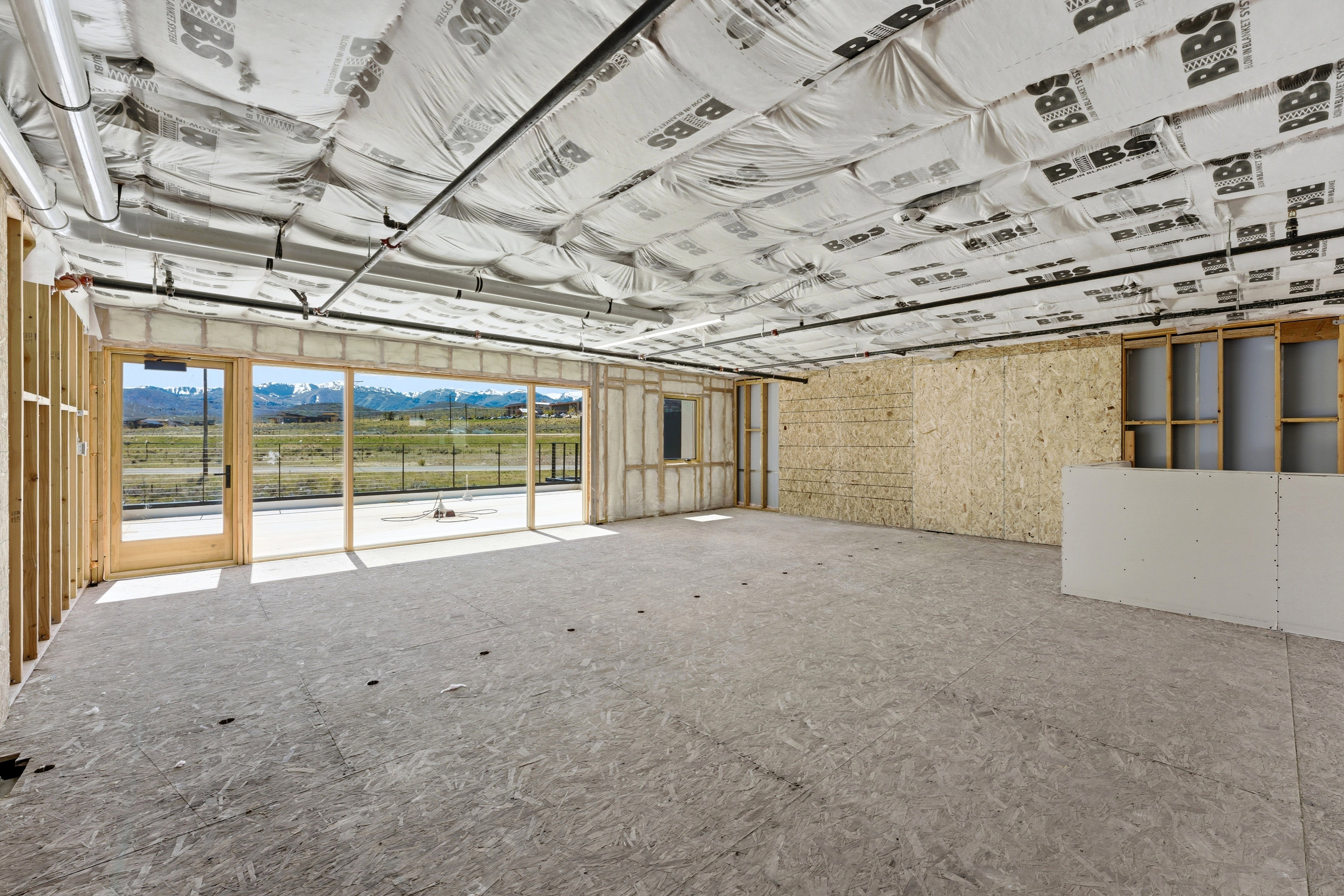 Open-concept interior space featuring exposed structural elements, a wood-framed glass door, and expansive windows