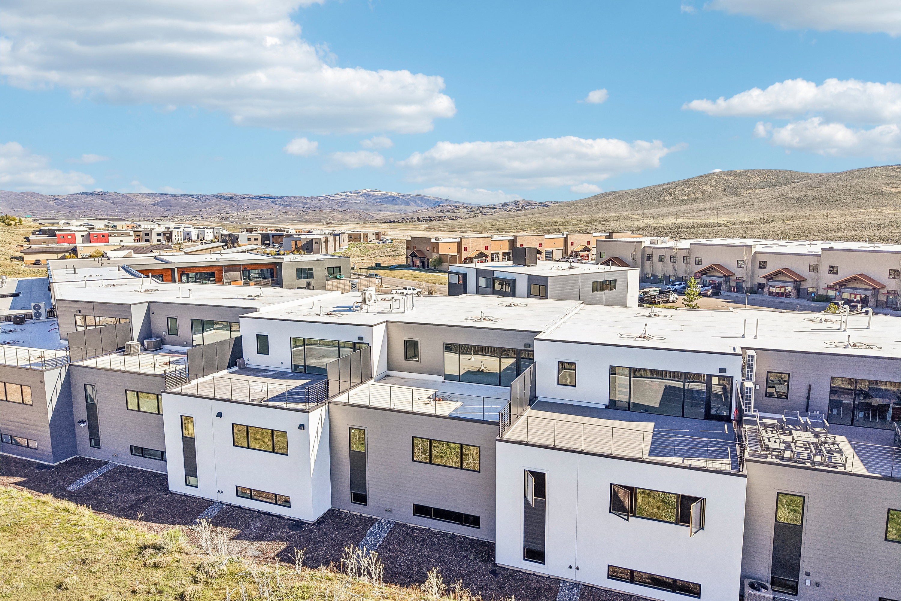 Modern multi-level townhome featuring a flat roofline, white and grey exterior paneling, and multiple private outdoor terrace spaces