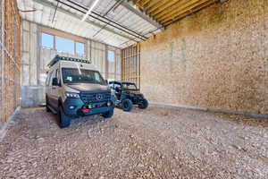 Spacious unfinished interior featuring high ceilings with exposed wood beams, multiple upper windows, insulation along one wall, and a gravel floor