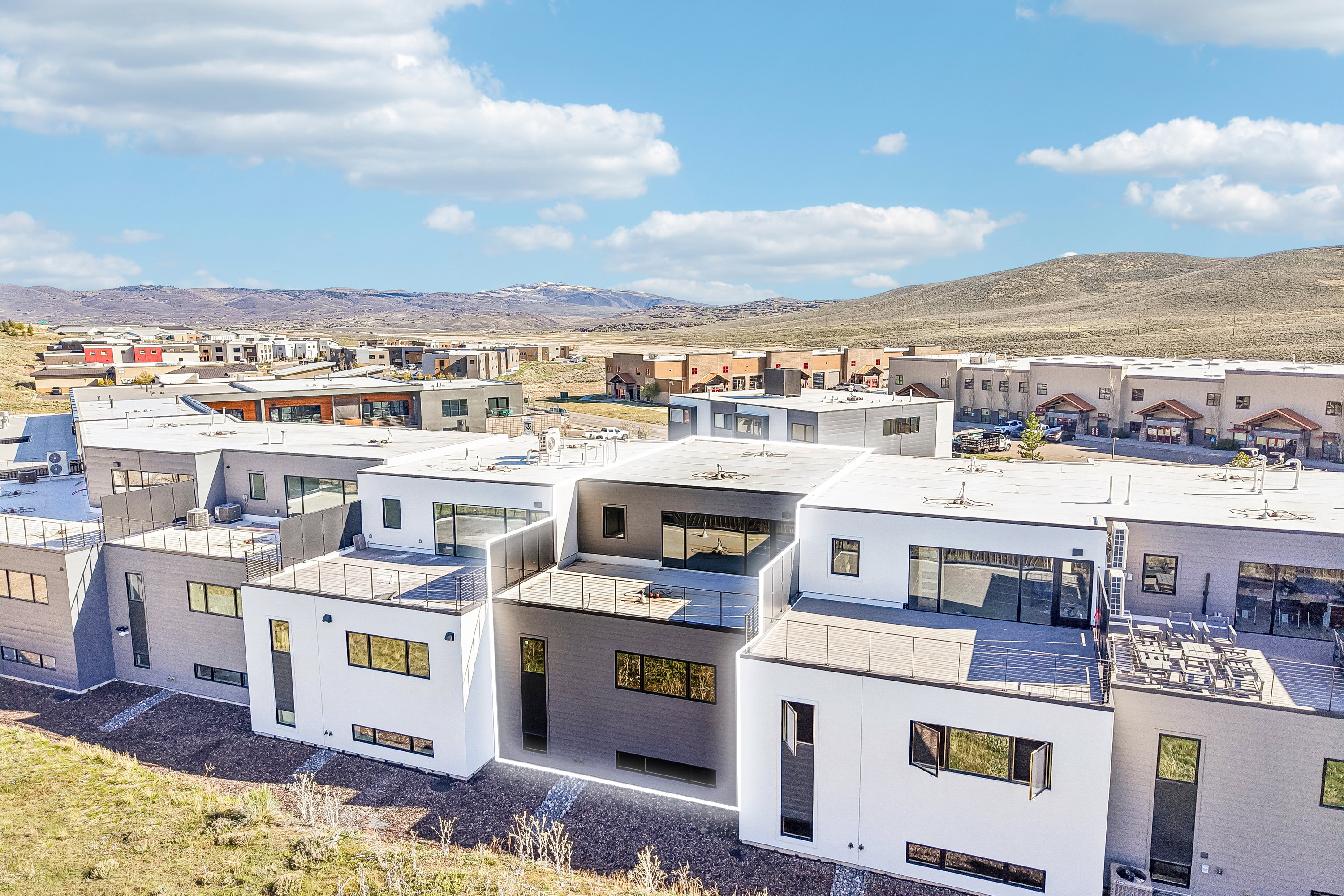 Modern multi-level exterior featuring white and charcoal-toned siding, expansive windows, flat roofs, and outdoor terrace spaces