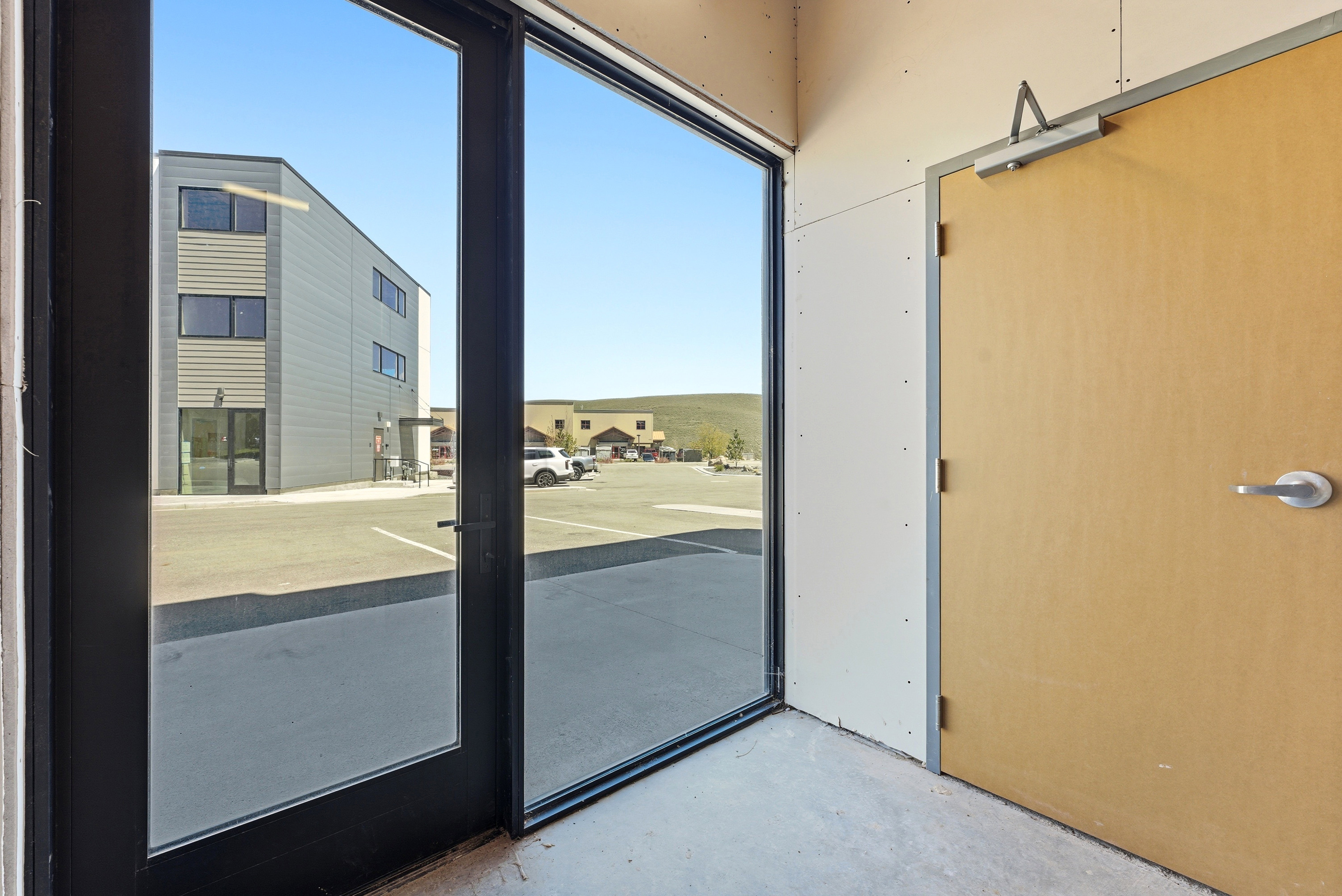 Full-light commercial entry door, adjacent interior wood-finish door with silver-tone hardware, and unfinished interior wall