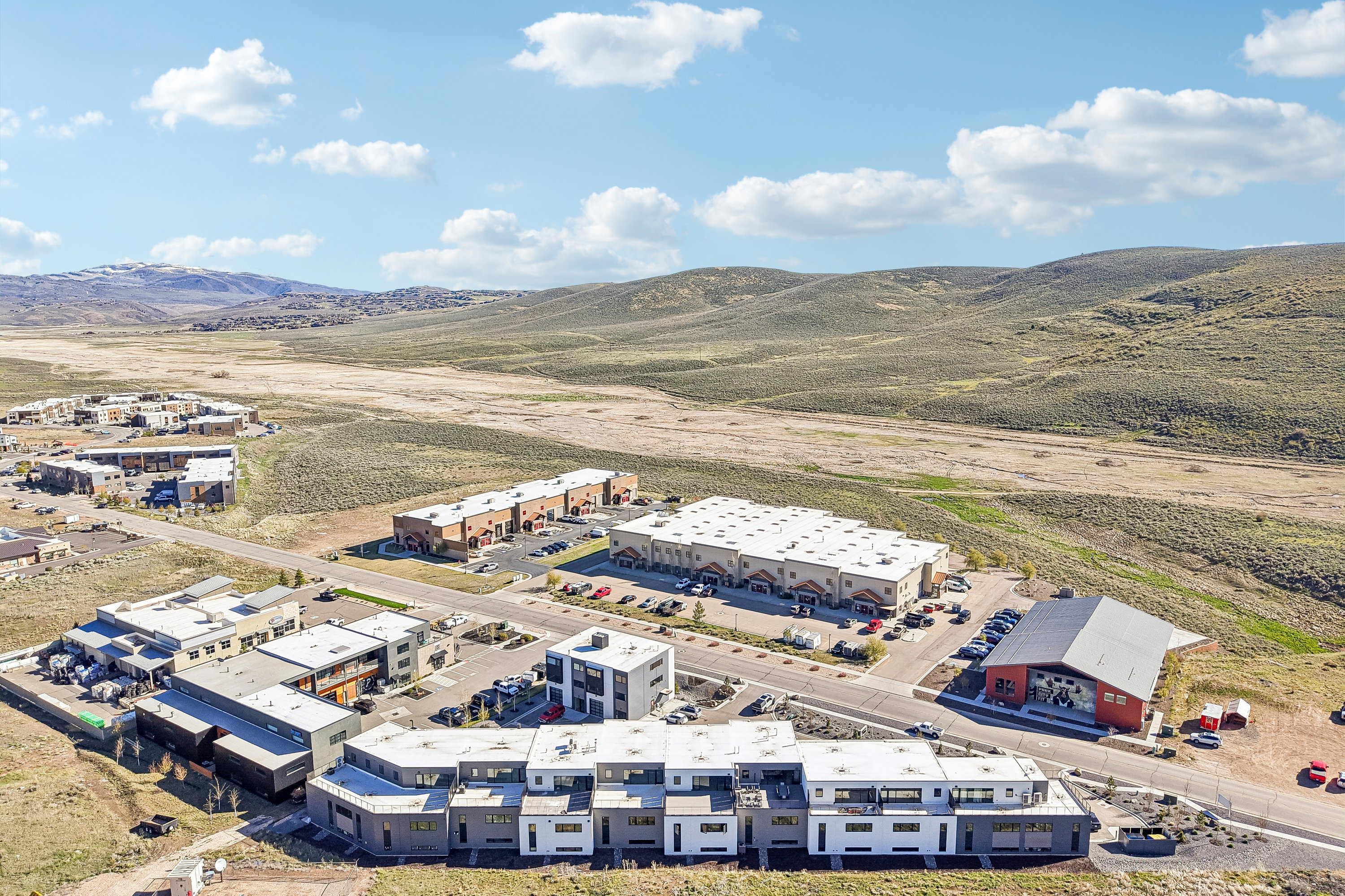 Aerial perspective showcasing a residential and commercial development situated amidst undulating natural terrain