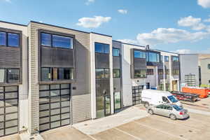 Modern multi-level exterior featuring light gray horizontal siding, dark accent panels, large windows, and contemporary glass panel garage doors