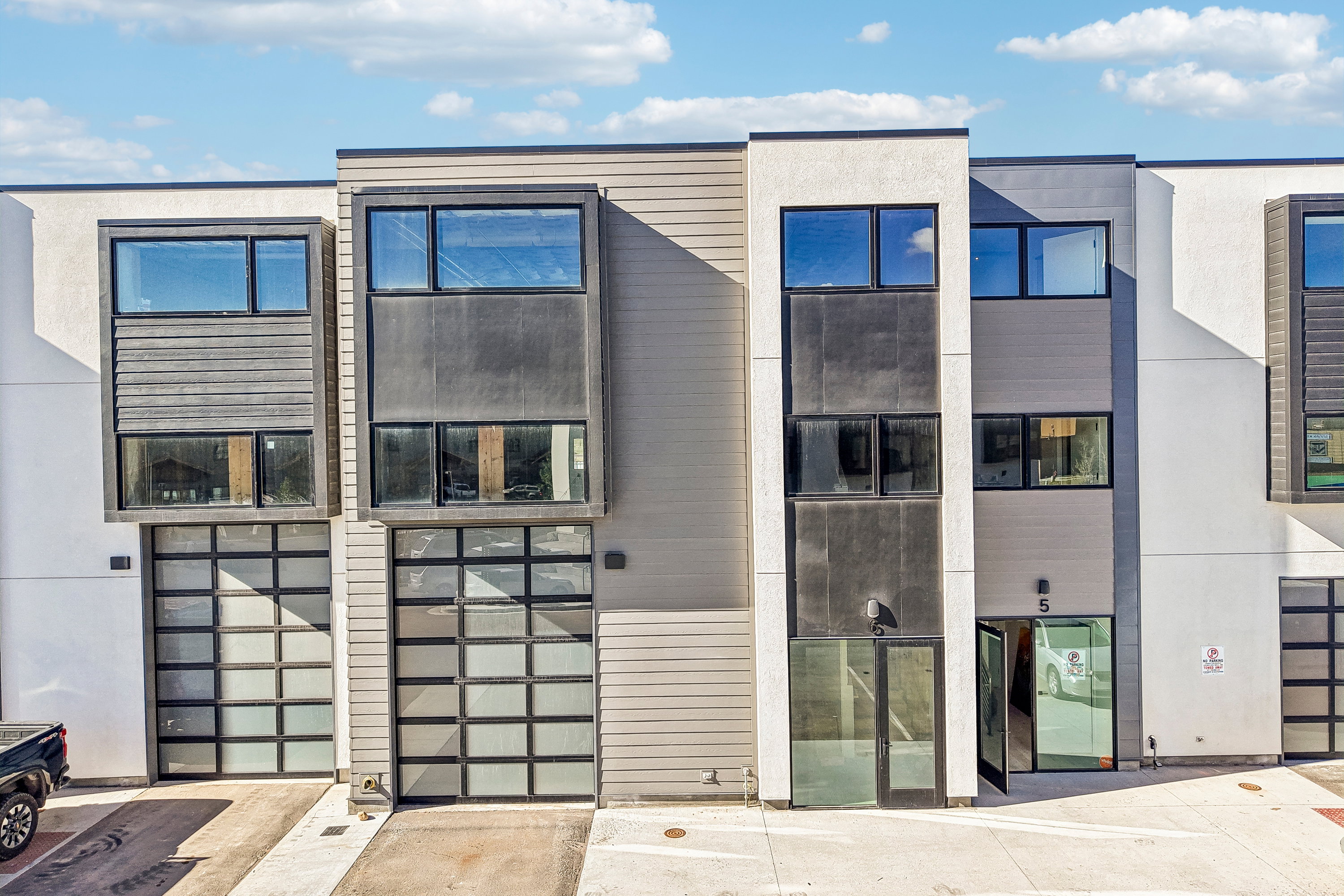 Contemporary townhouse facade featuring large windows, multi-textured siding, and modern glass-paneled garage doors