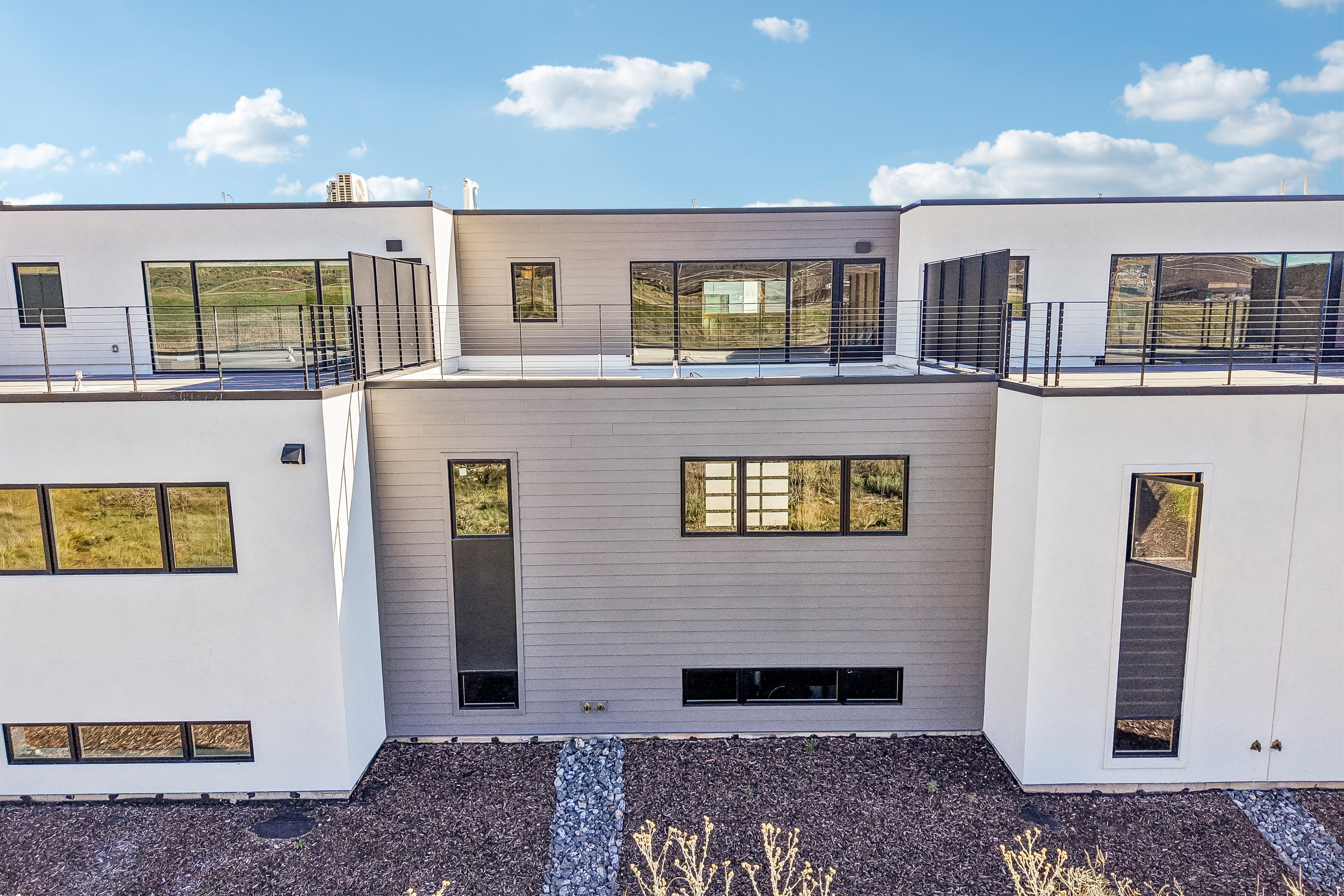 Modern architectural exterior featuring multiple balconies with metal railings, large windows, and contrasting white and gray siding