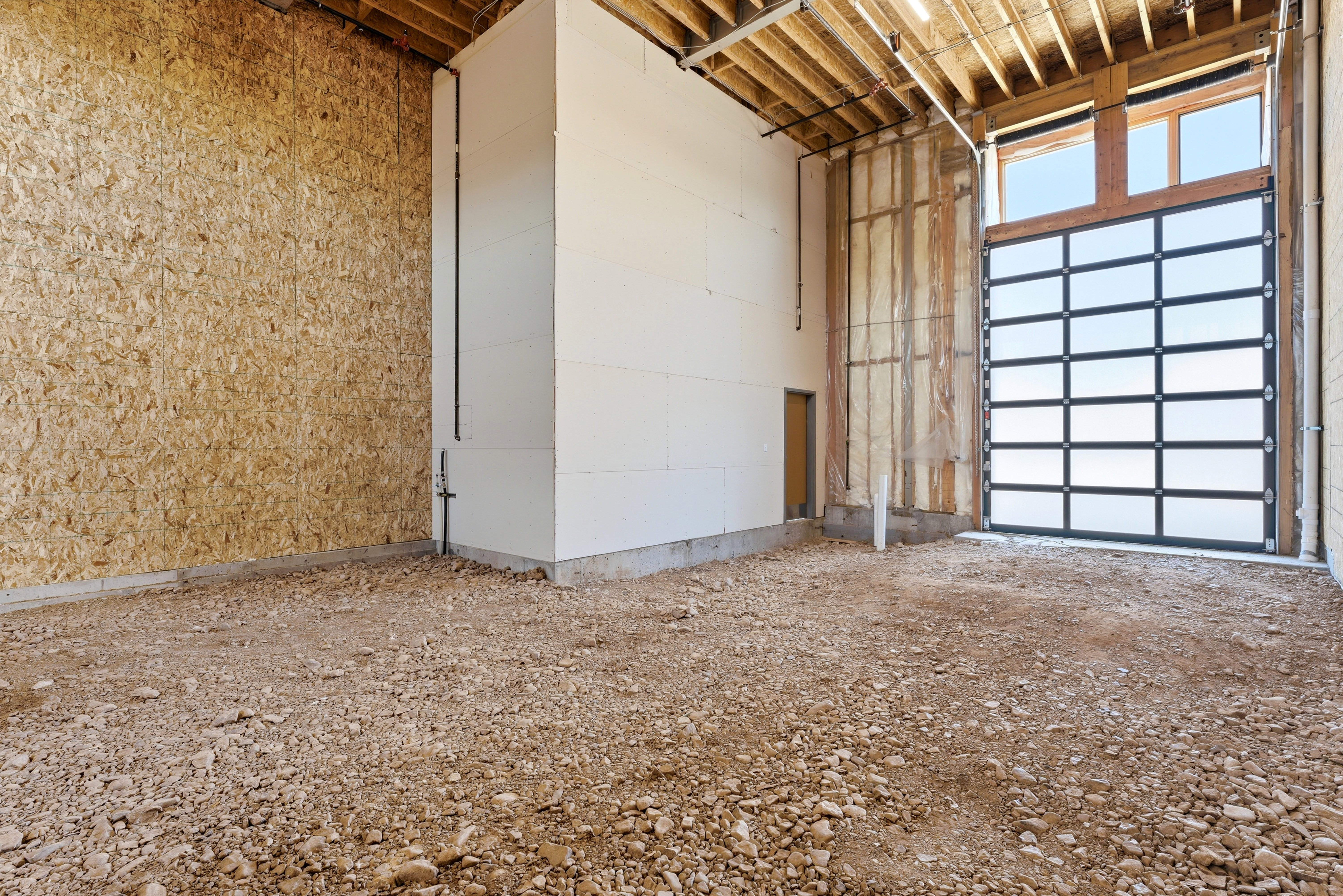 Spacious unfinished interior featuring an overhead garage door with frosted glass panels and an exposed wood beam ceiling