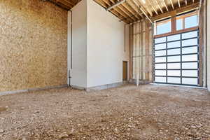 Spacious unfinished interior featuring an overhead garage door with frosted glass panels and an exposed wood beam ceiling