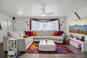 Spacious living area featuring wood-finish flooring, a ceiling fan, and a front entry door with a decorative glass insert