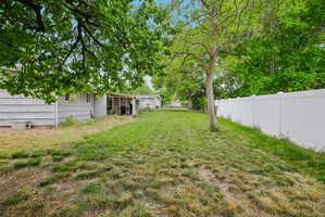 Expansive backyard featuring a white privacy fence, mature trees, and a covered patio area