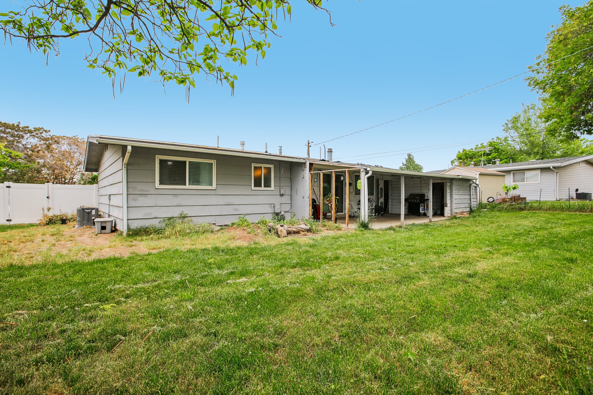 Expansive grass lawn featuring a rear house facade with horizontal siding, multiple windows, a covered patio, and a privacy fence