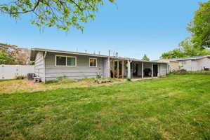 Expansive grass lawn featuring a rear house facade with horizontal siding, multiple windows, a covered patio, and a privacy fence